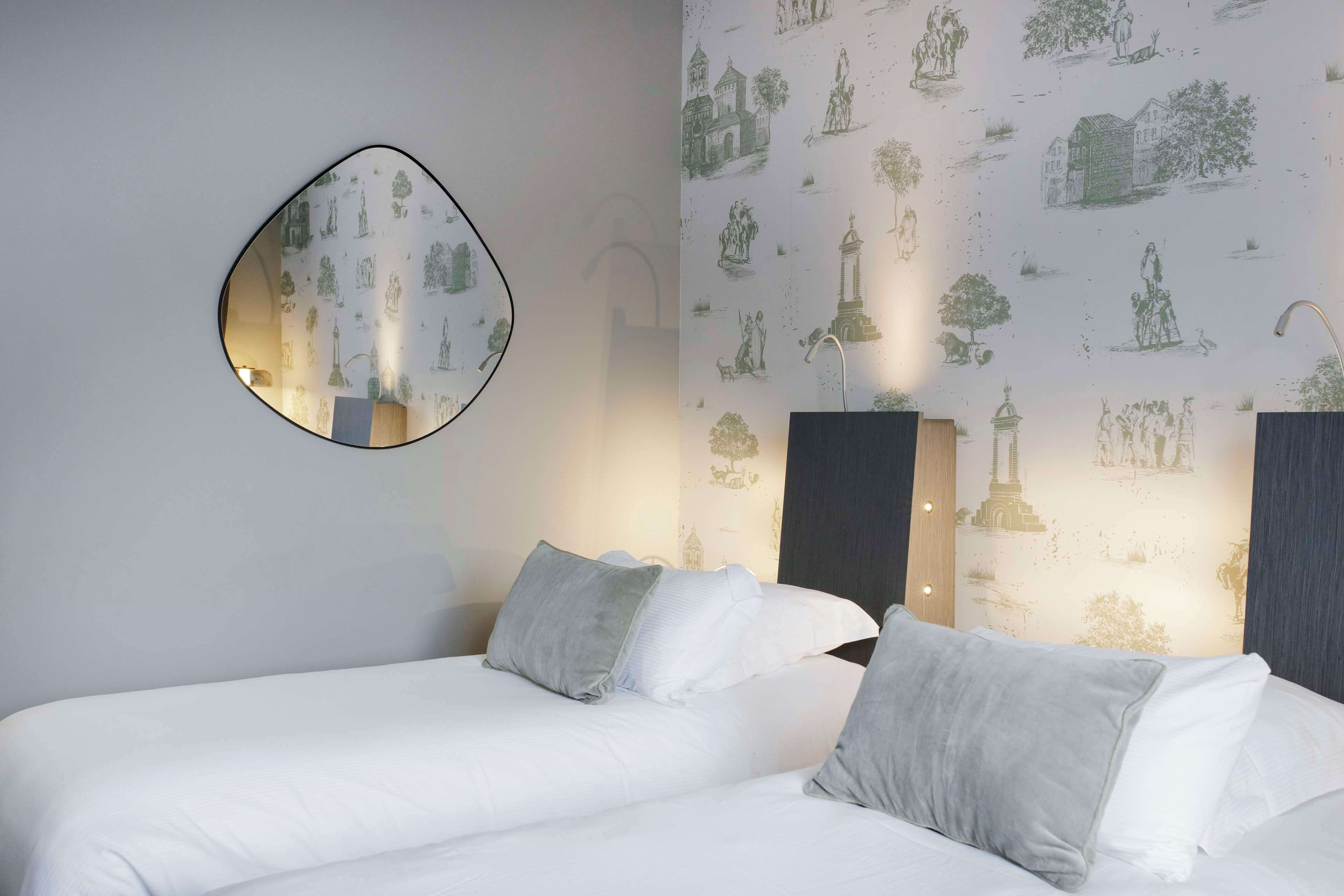 A hotel room with a bed, two bedside tables, a wall-mounted mirror, and a wallpaper with architectural illustrations.
