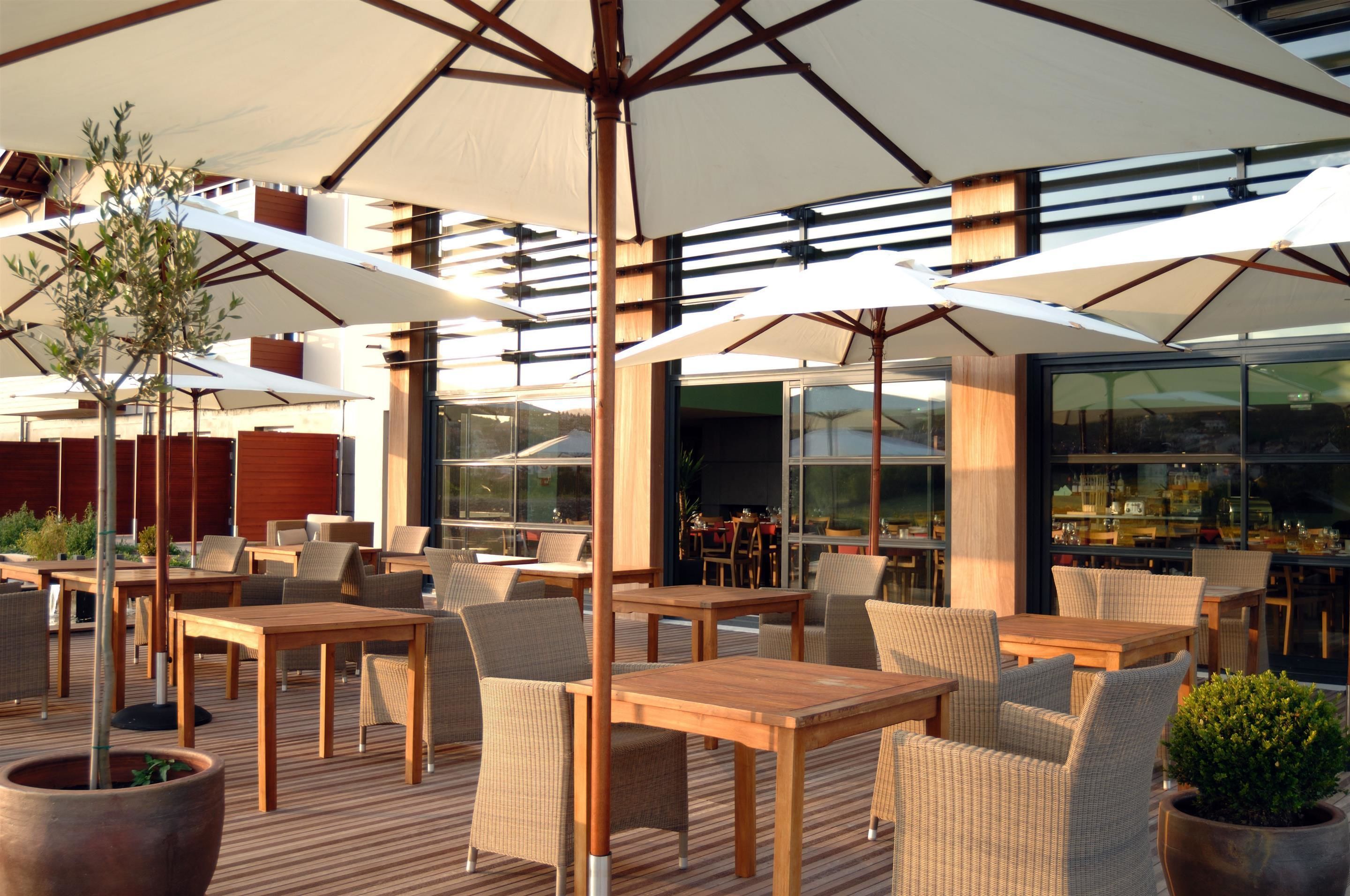 An outdoor seating area with tables and chairs, large umbrellas, and potted plants.