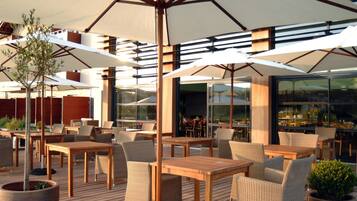 An outdoor seating area with tables and chairs, large umbrellas, and potted plants.