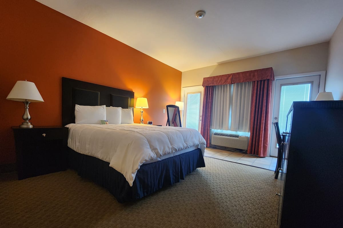 A hotel room with a large bed, two bedside tables with lamps, a window with curtains, and an air conditioning unit.