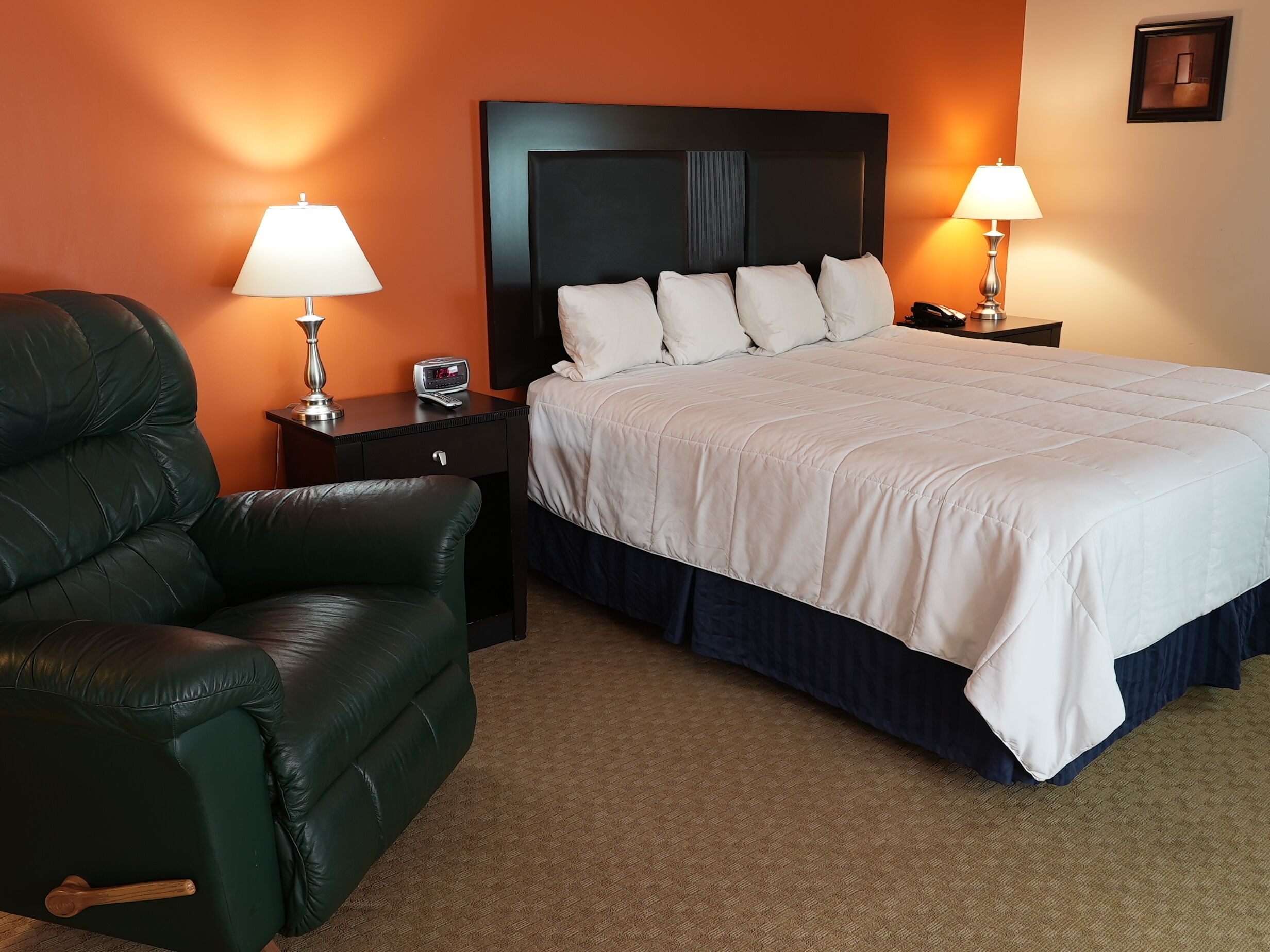 Une chambre d’hôtel avec un lit, un fauteuil en cuir vert, deux tables de chevet avec des lampes et une horloge posée sur l’une des tables.