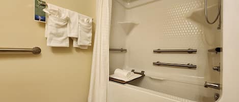 A bathroom with a bathtub, a shower, and a toilet. There are handrails and a towel rack with towels.