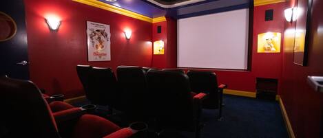 Cine con asientos rojos, una pantalla grande y apliques de pared.