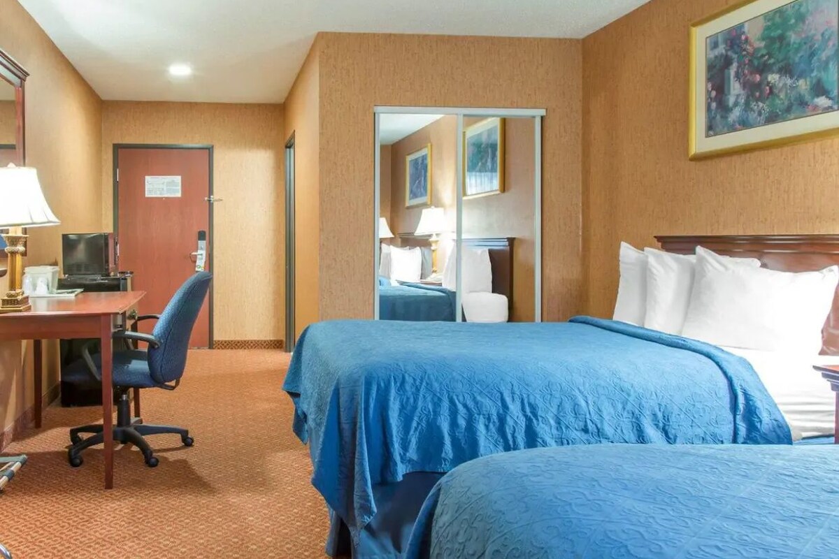 Une chambre d’hôtel avec deux lits, un bureau avec un ordinateur et une chaise.