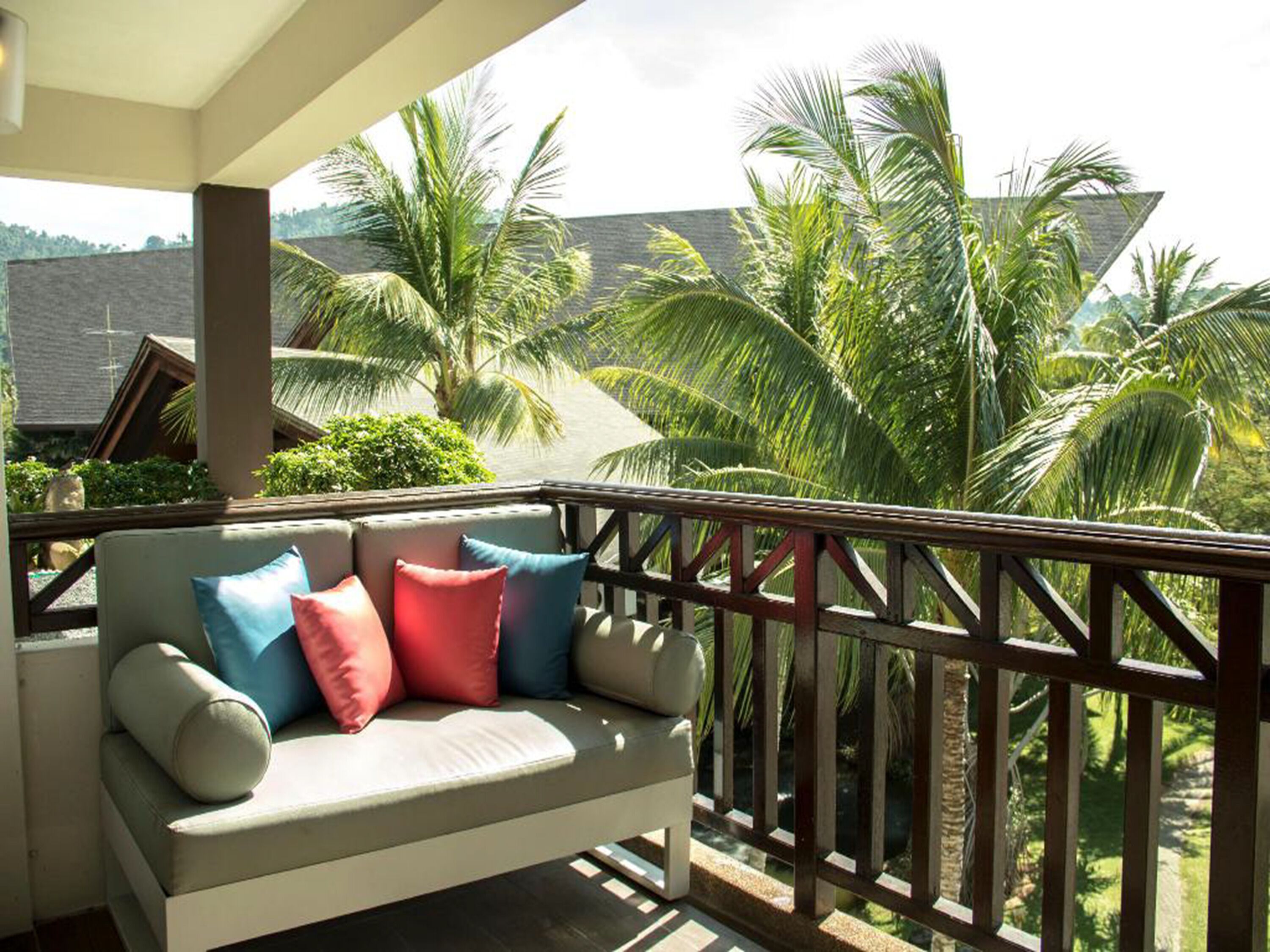 Ein Balkon mit einer Couch und Kissen, mit Blick auf Palmen und ein Gebäude.