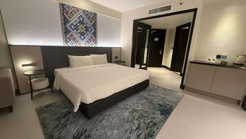 A modern hotel room with a large bed, bedside tables, a desk, and a bathroom visible through an open door.