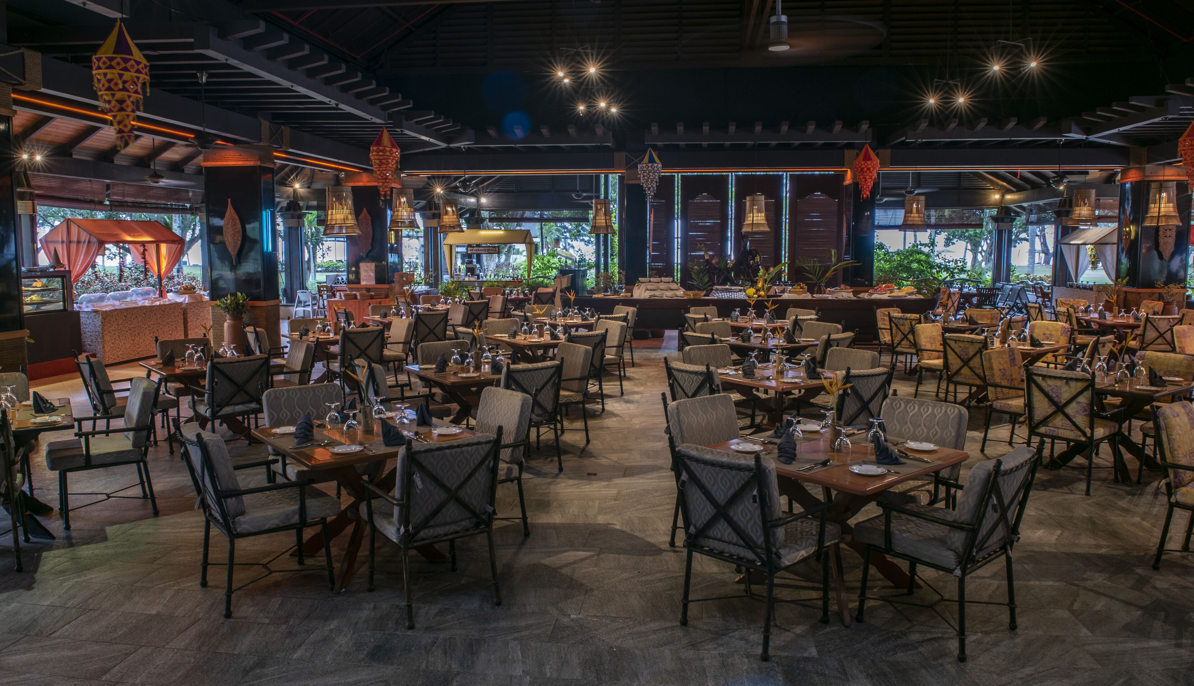 A spacious restaurant with multiple dining tables and chairs, ambient lighting, and decorative lanterns.