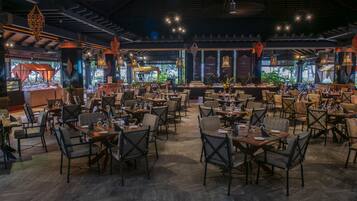 A spacious restaurant with multiple dining tables and chairs, ambient lighting, and decorative lanterns.