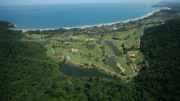 Vue aérienne d’un terrain de golf situé sur la côte, avec plusieurs étangs, une plage et une zone résidentielle.