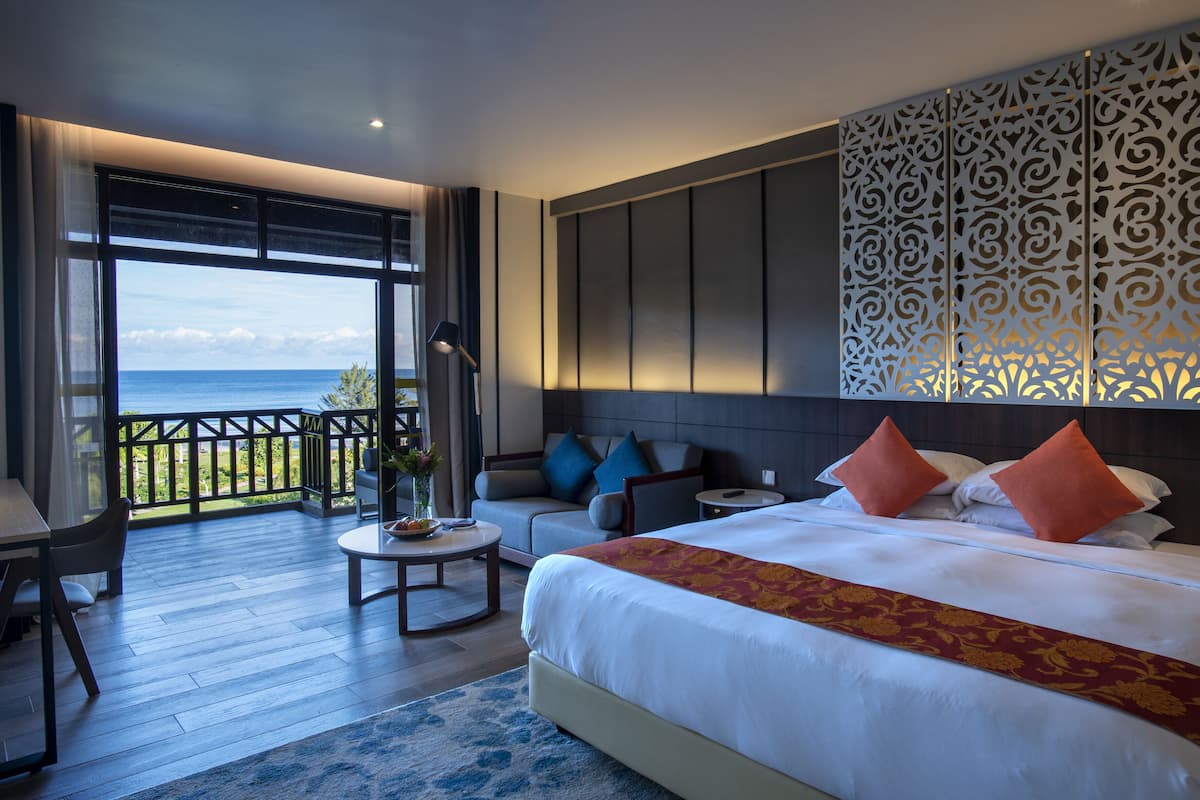 Ein Hotelzimmer mit einem großen Bett, einer Sitzecke mit Tisch und einem Balkon mit Meerblick.