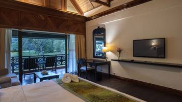 A room with a large bed, a dining table with chairs, a TV mounted on the wall, and a view of the outdoors through a large window.