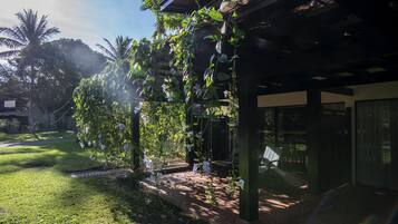 A covered outdoor area with a pergola structure, a grassy lawn, and a palm tree in the background.