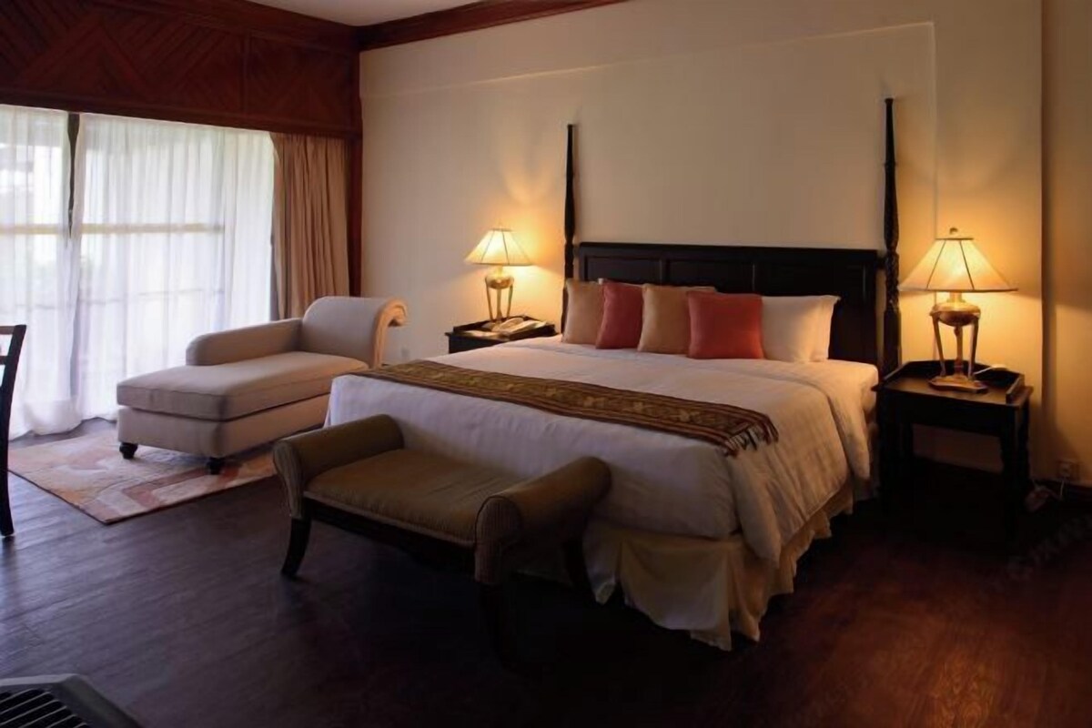 Une chambre d’hôtel avec un grand lit, deux tables de chevet avec des lampes, un canapé et un fauteuil.