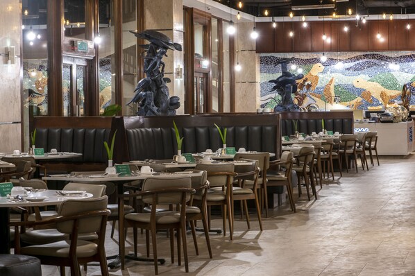 Un restaurant avec des banquettes et des tables, un mur décoré de mosaïques et une sculpture représentant une créature marine.