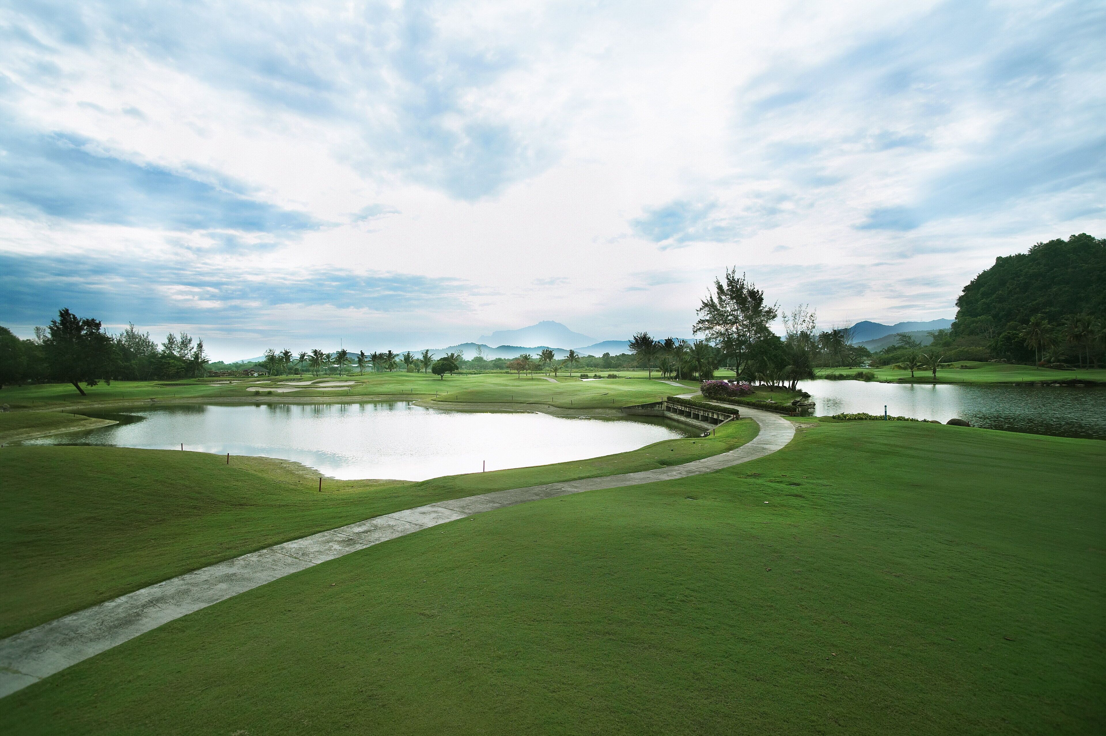 A golf course with a pond, pathways, and distant mountains.