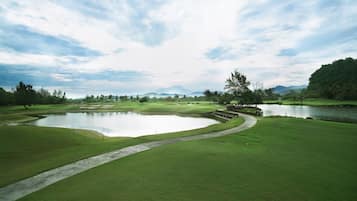 A golf course with a pond, pathways, and distant mountains.