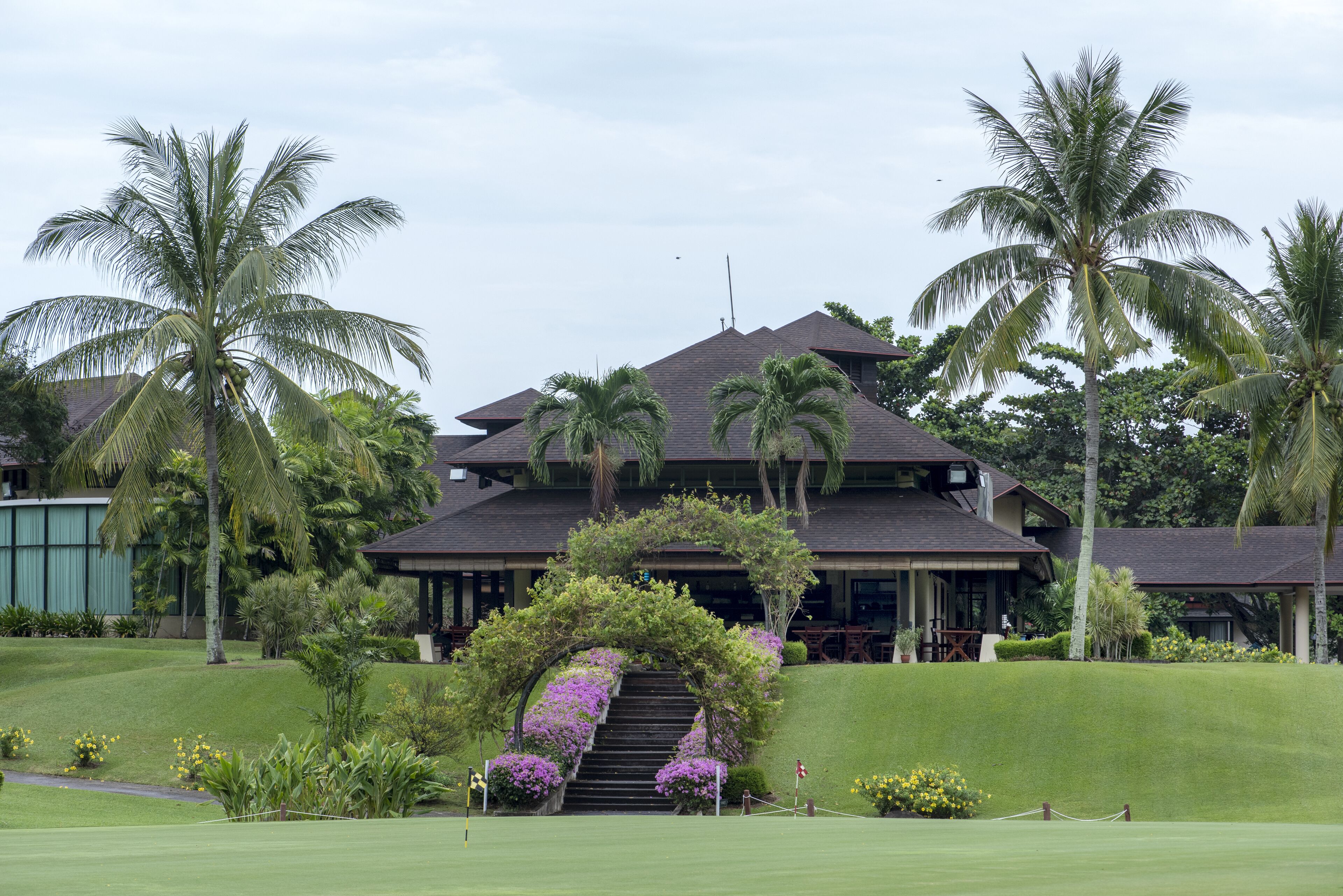 A two-story building with a covered entrance, surrounded by palm trees and a well-maintained lawn.