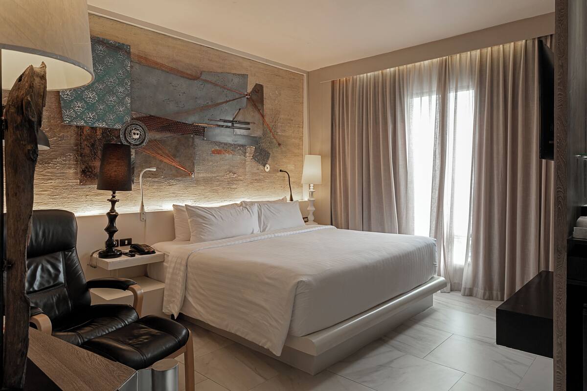 A modern hotel room with a large bed, a desk, a chair, and a wall-mounted TV.