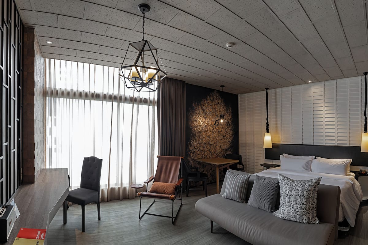 A hotel room with a bed, a sofa, a chair, a small table, and a wall with a textured pattern.