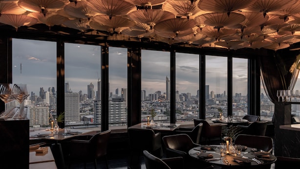 Un restaurante con vistas a la ciudad, amplias ventanas y un techo con lámparas colgantes.