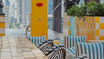 Un bar en la azotea con vistas a la ciudad, asientos a rayas y un pilar amarillo.