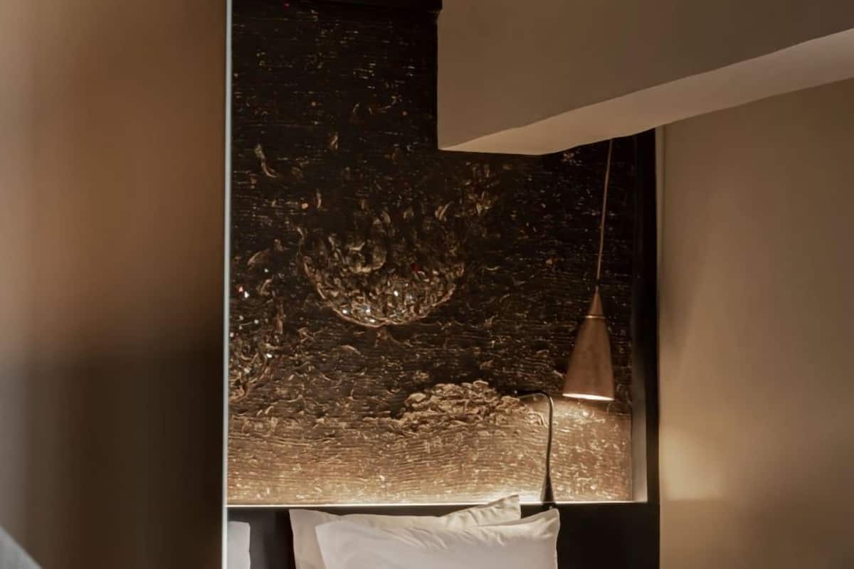 A modern hotel room with a bed, a desk, a chair, and a decorative wall.