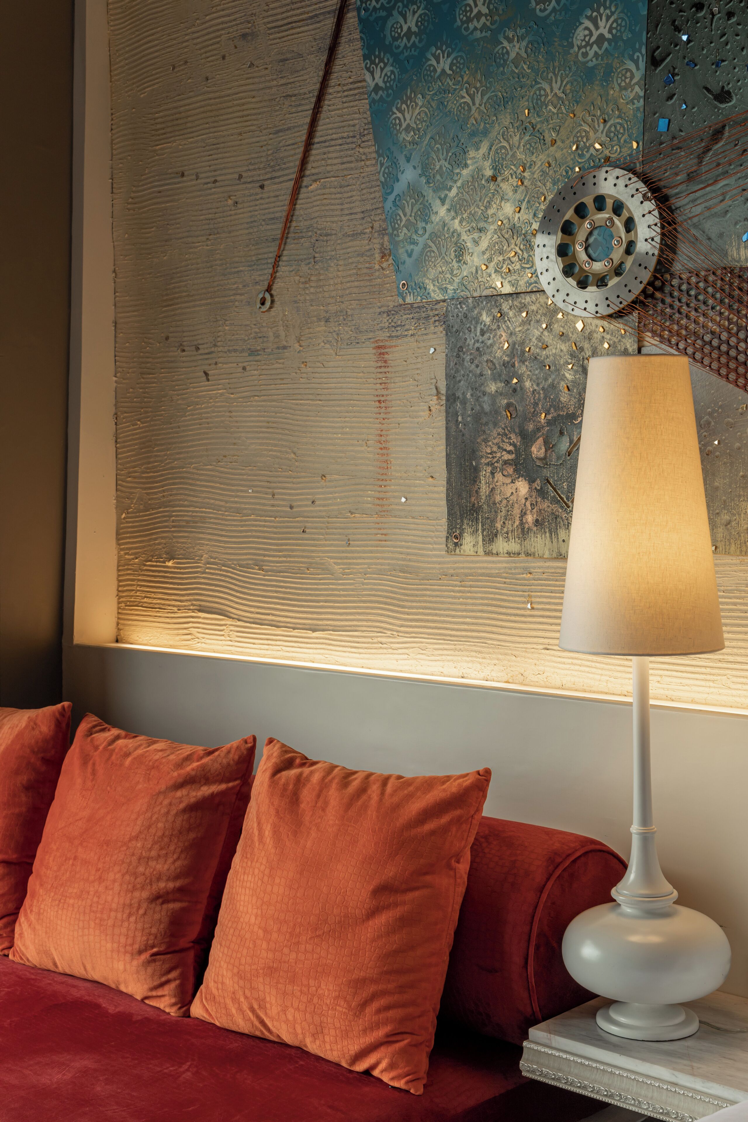 A room with a red sofa, a white lamp, and a wall with a decorative metal plate and patterned wallpaper.