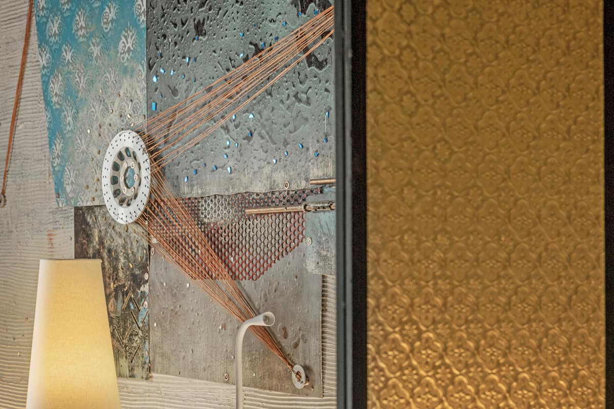 A hotel room with a bed, a lamp, a window with a view, and a textured wall.