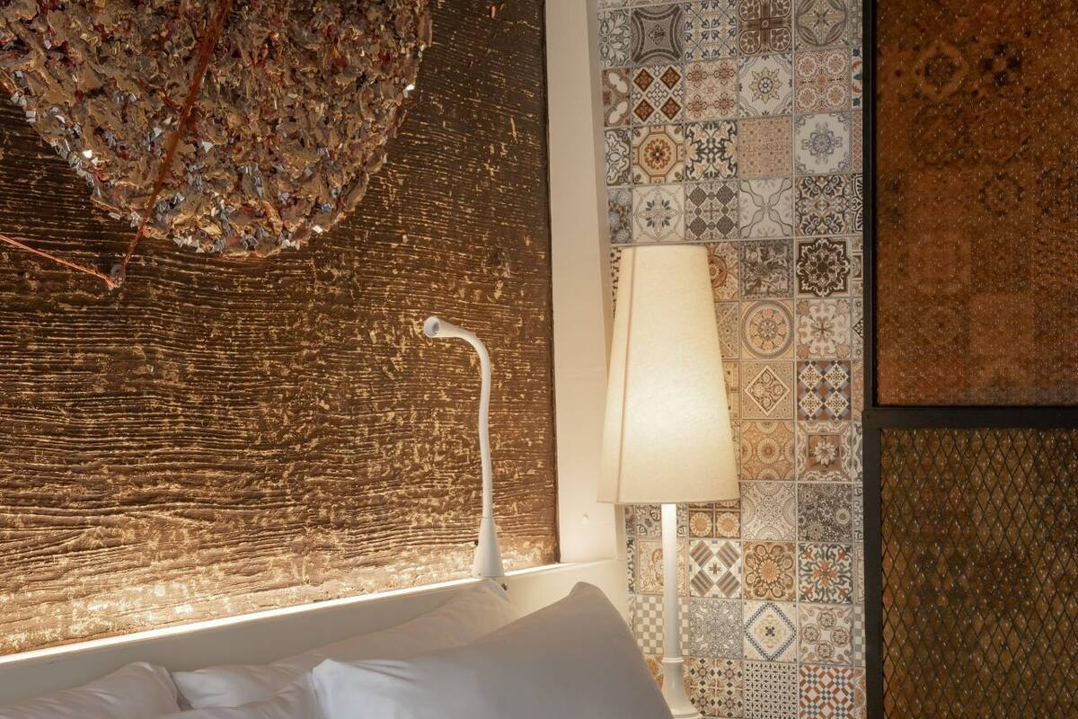 A hotel room with a bed, a lamp, and a wall with patterned tiles.
