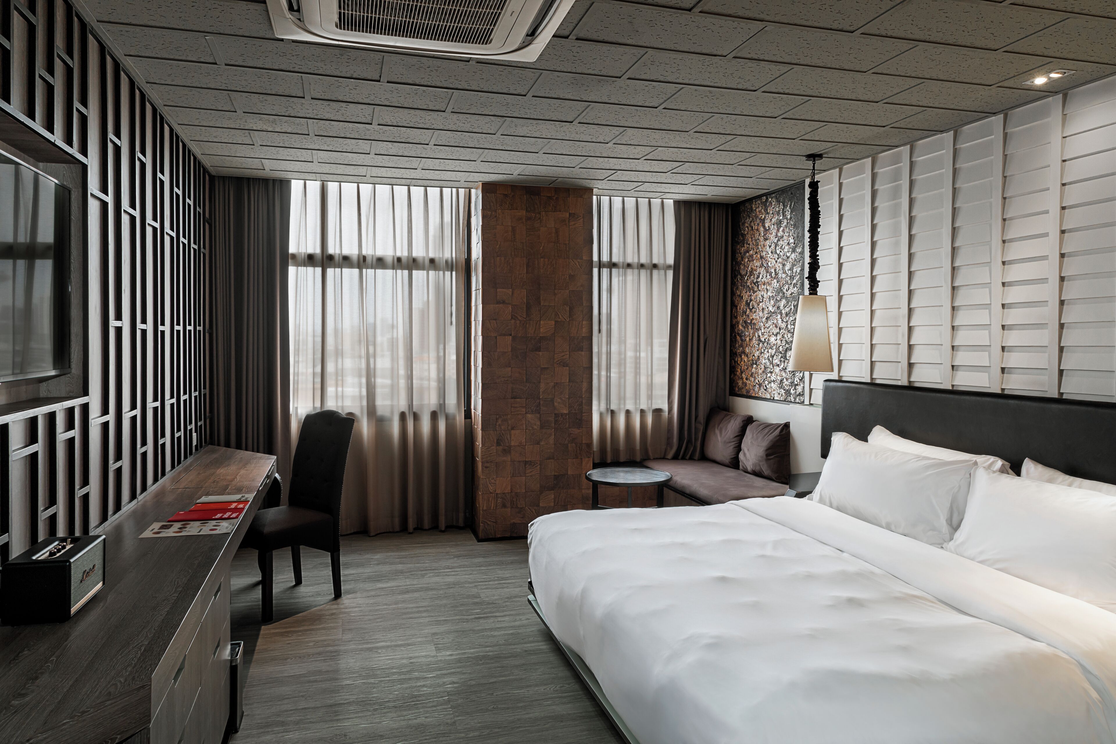A modern hotel room with a large bed, a desk, a chair, a small round table, and a large window with curtains.