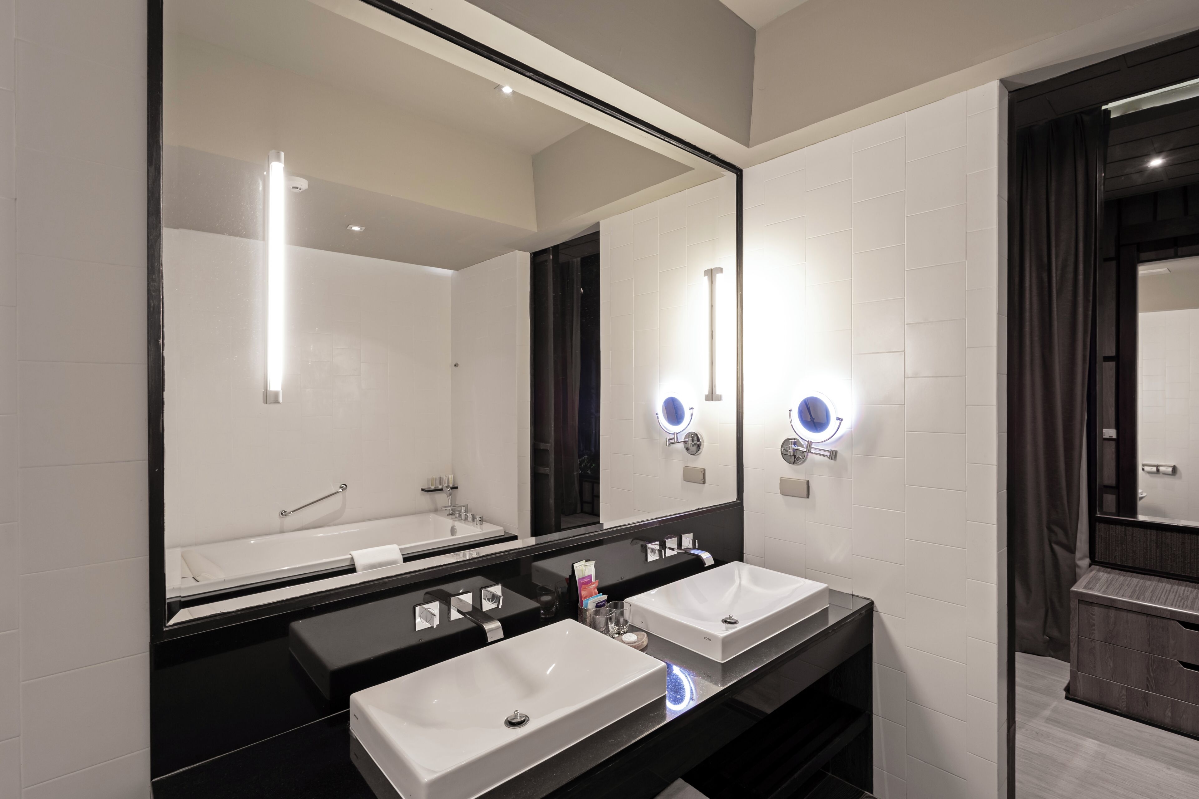 A modern bathroom with two sinks, a large mirror, and a bathtub.