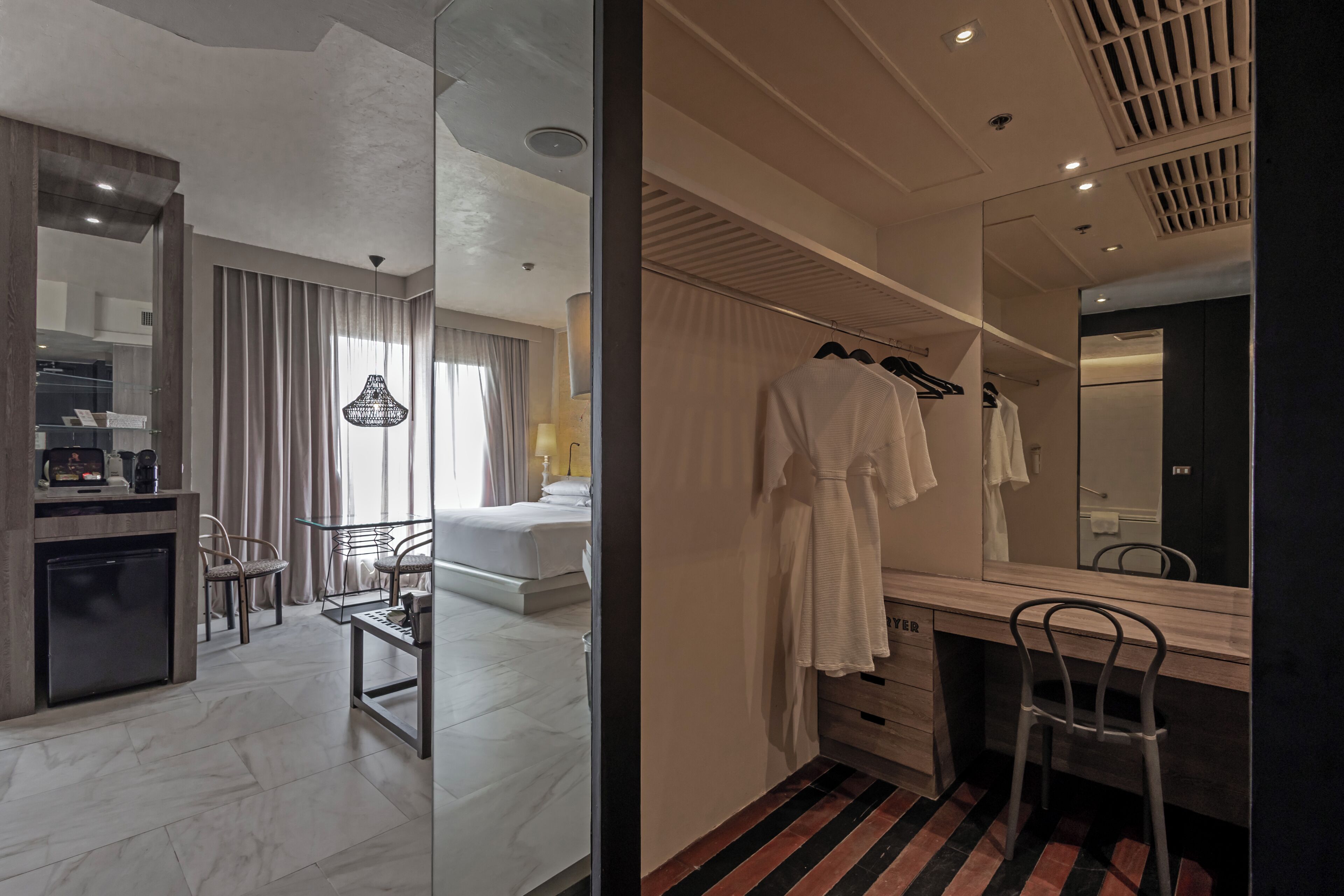 A modern hotel room with a bed, a desk, a chair, a mirror, and a wardrobe.
