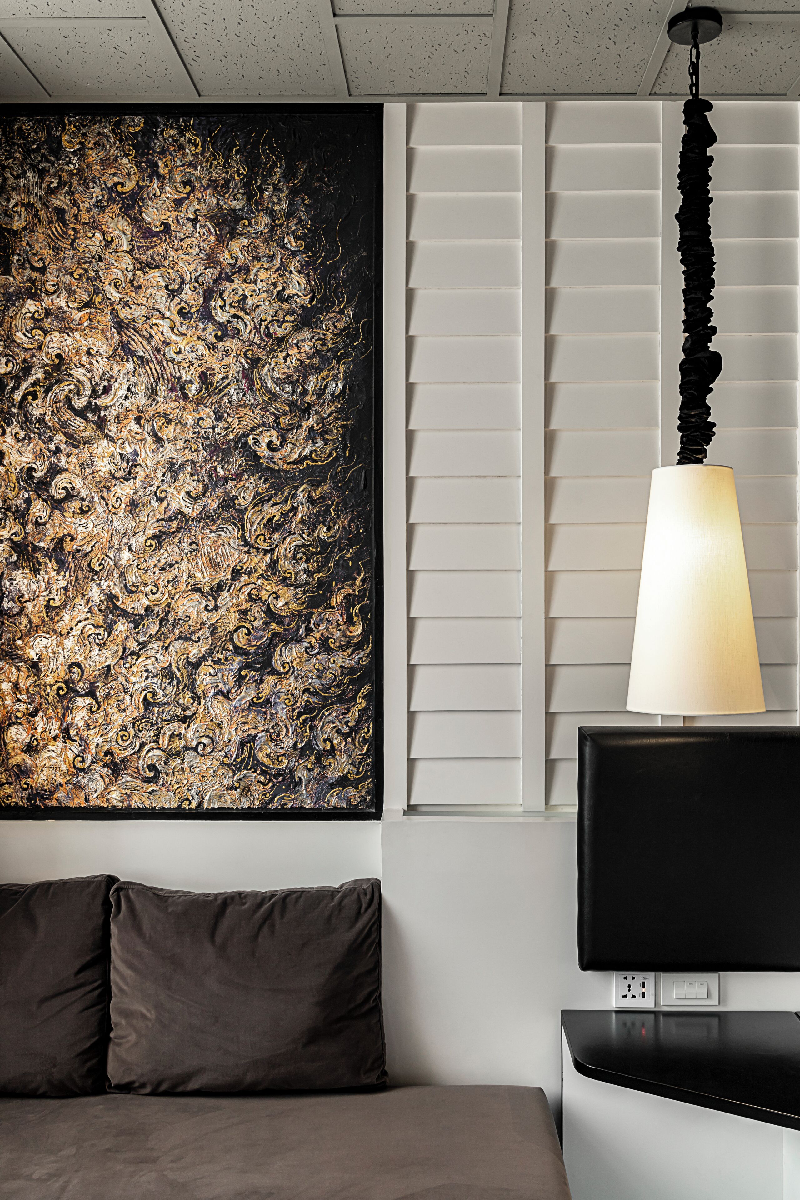 A room with a large abstract painting, a black TV stand, and a hanging lamp.