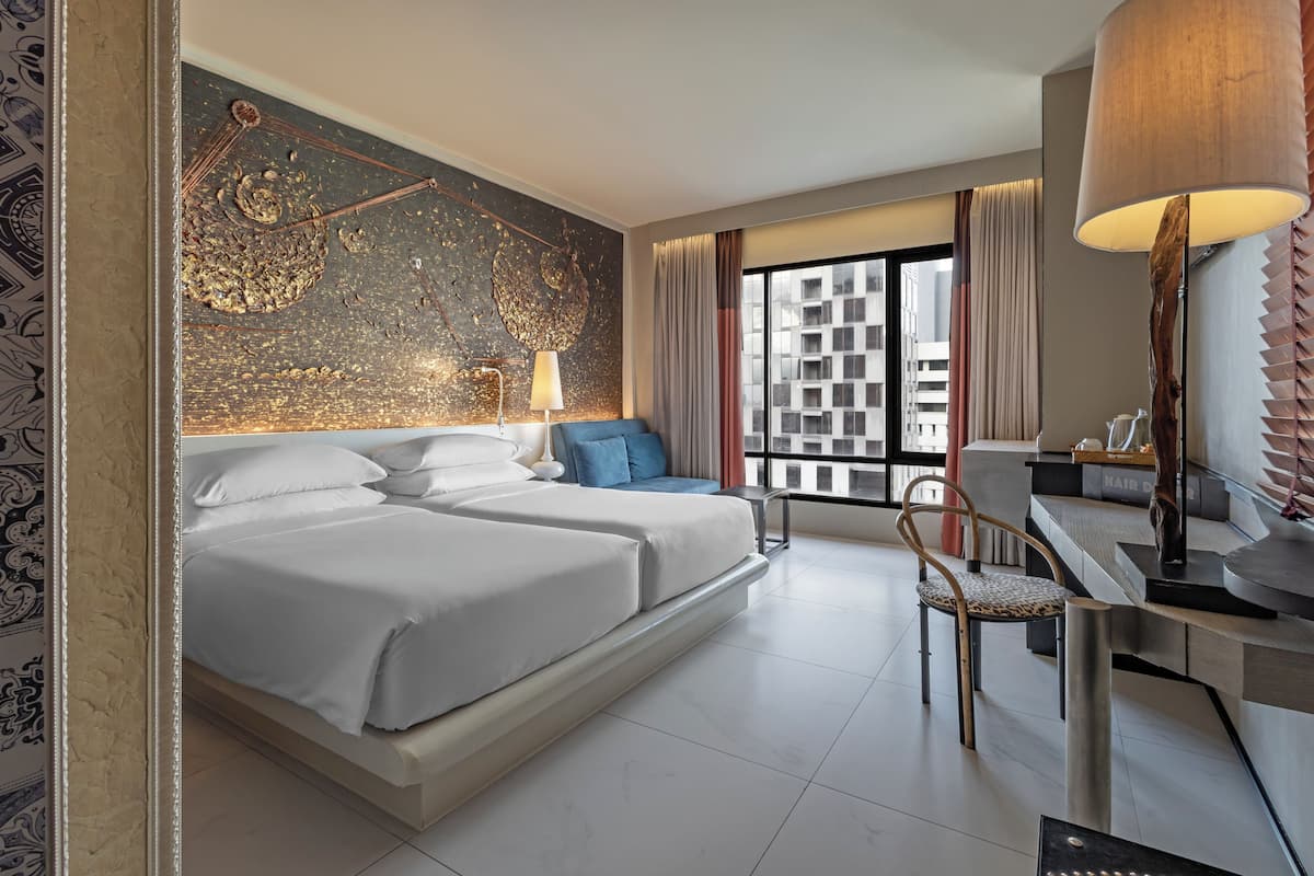 A modern hotel room with a large bed, a desk, a chair, and a view of the city.