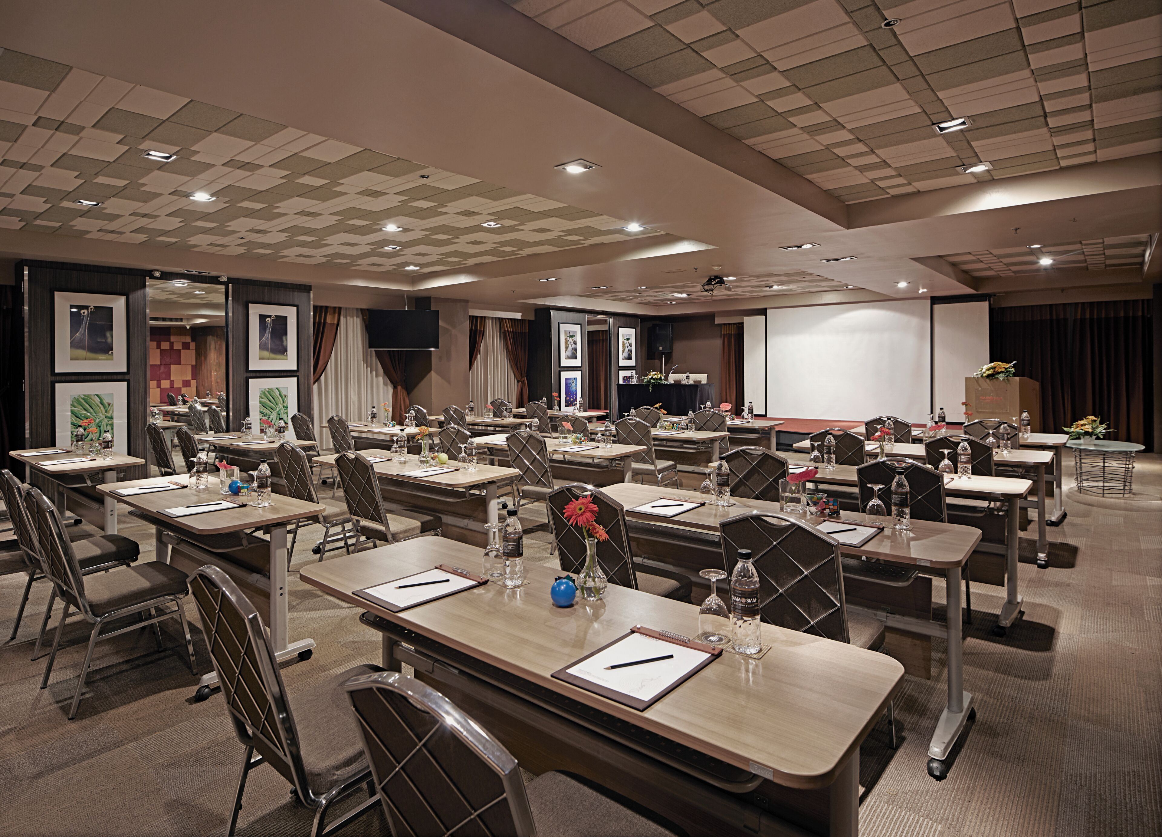 A conference room with multiple tables, chairs, and a presentation screen.