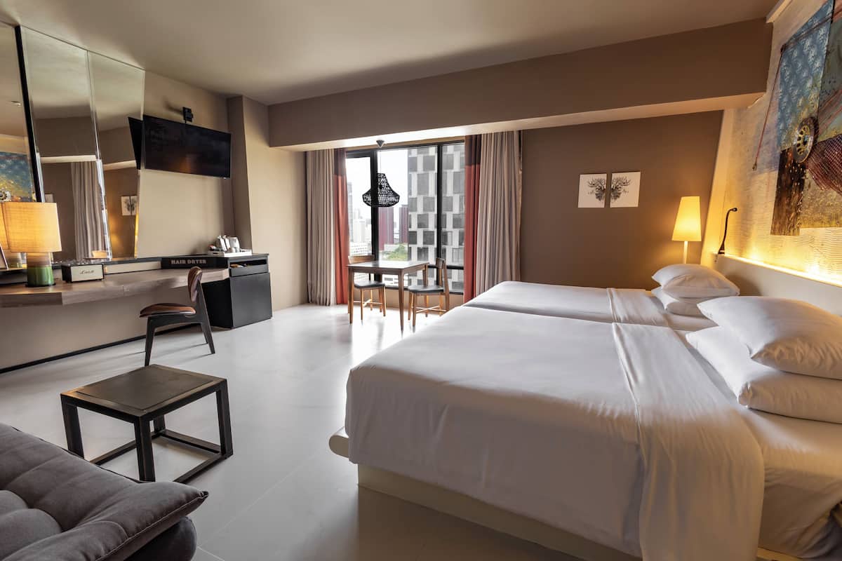 A hotel room with a large bed, a desk, a chair, a small table, and a balcony with a view.