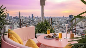 Un balcón con un sofá rosa, una mesa redonda y dos vasos de cerveza.