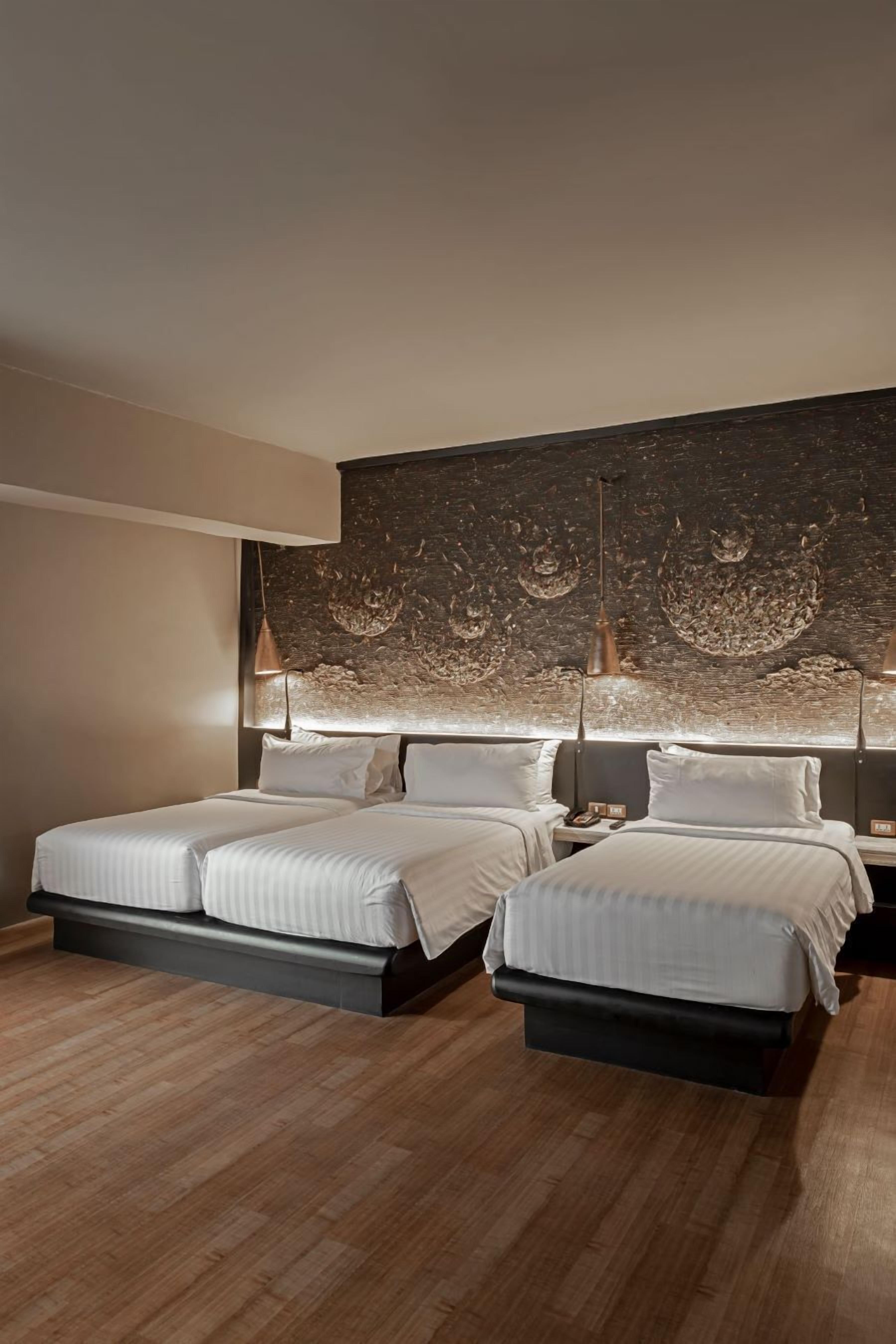 A modern hotel room with two beds, a large wall mural, and pendant lighting.