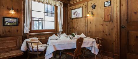 A wooden dining room with a round table set for four, white tablecloths, and wooden chairs.