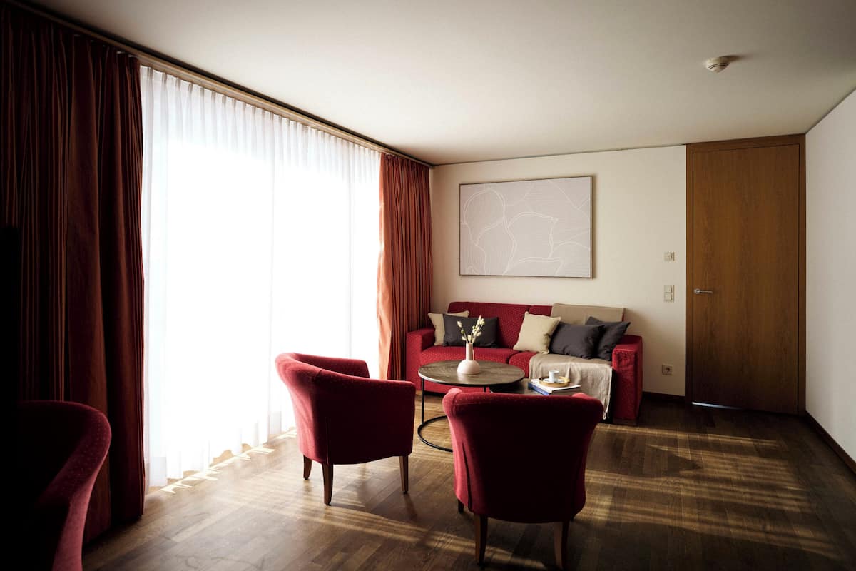 A modern living room with a red sofa, two red armchairs, a coffee table, and a wooden door.