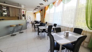 A modern dining area with a bar, white-tiled floor, black chairs, and a view through large windows with sheer curtains. - Zirka Hotel (Odesa)