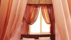 A bed with white linens, a dark headboard, and a window with sheer curtains. - Zirka Hotel (Odesa)