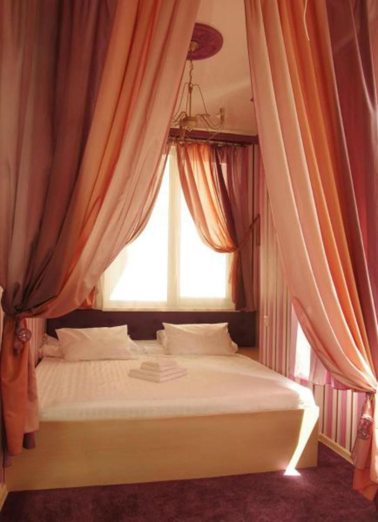 A bedroom with a bed, curtains, a window, and a nightstand.