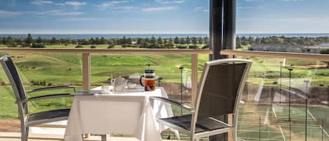 A balcony with a table and chairs, overlooking a golf course.