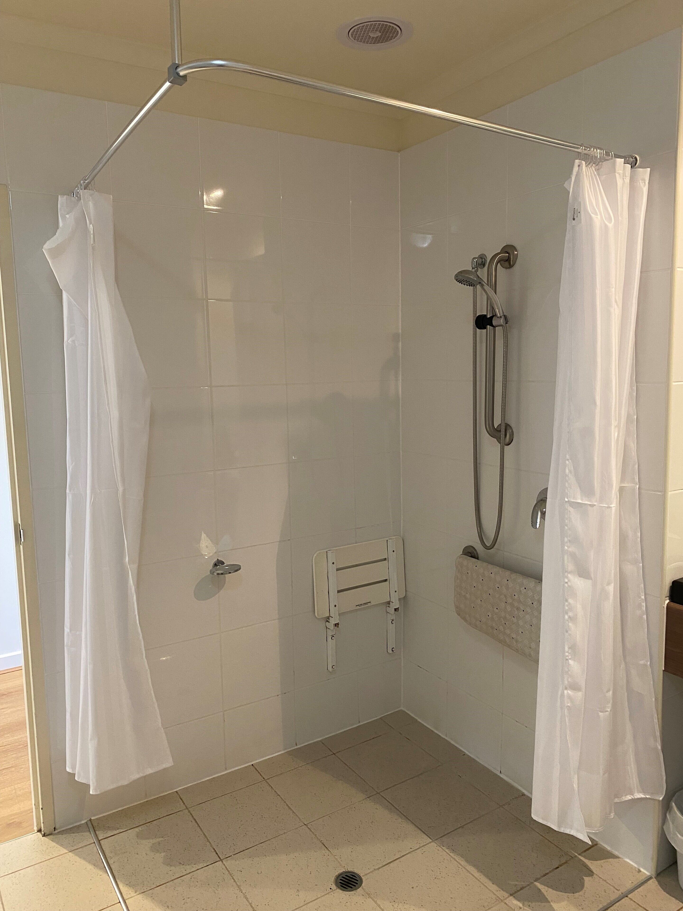 A walk-in shower with white tiled walls, a handheld showerhead, a handheld shower attachment, and a white shower curtain.