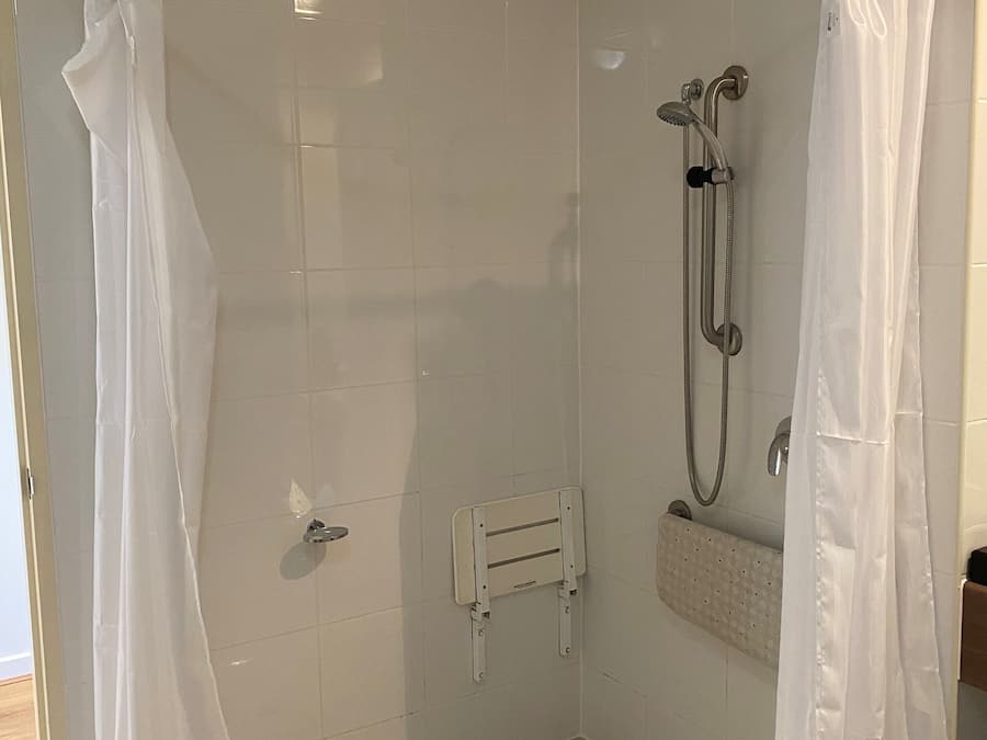 A walk-in shower with white tiled walls, a handheld showerhead, a handheld shower attachment, and a white shower curtain.