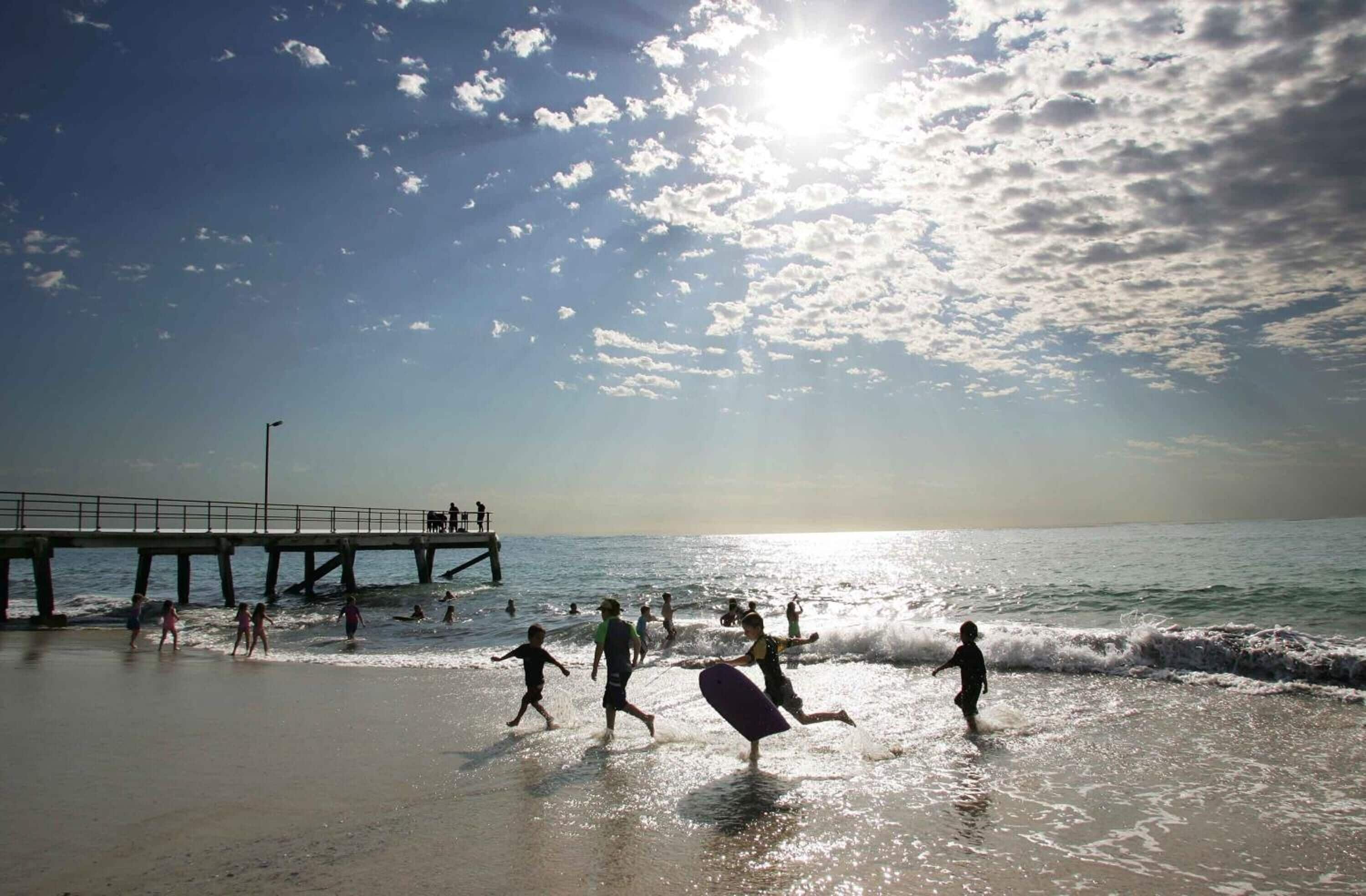 A beach scene with a pier, people walking along the shore, and waves crashing onto the beach.