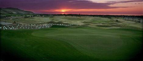 A golf course at sunset with a clear sky, well-maintained grass, and a few buildings in the background.