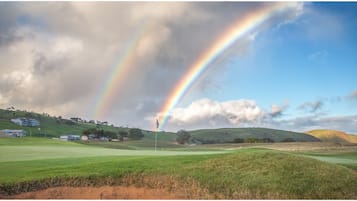 Un campo de golf con un arcoíris, casas en una colina y una bandera.