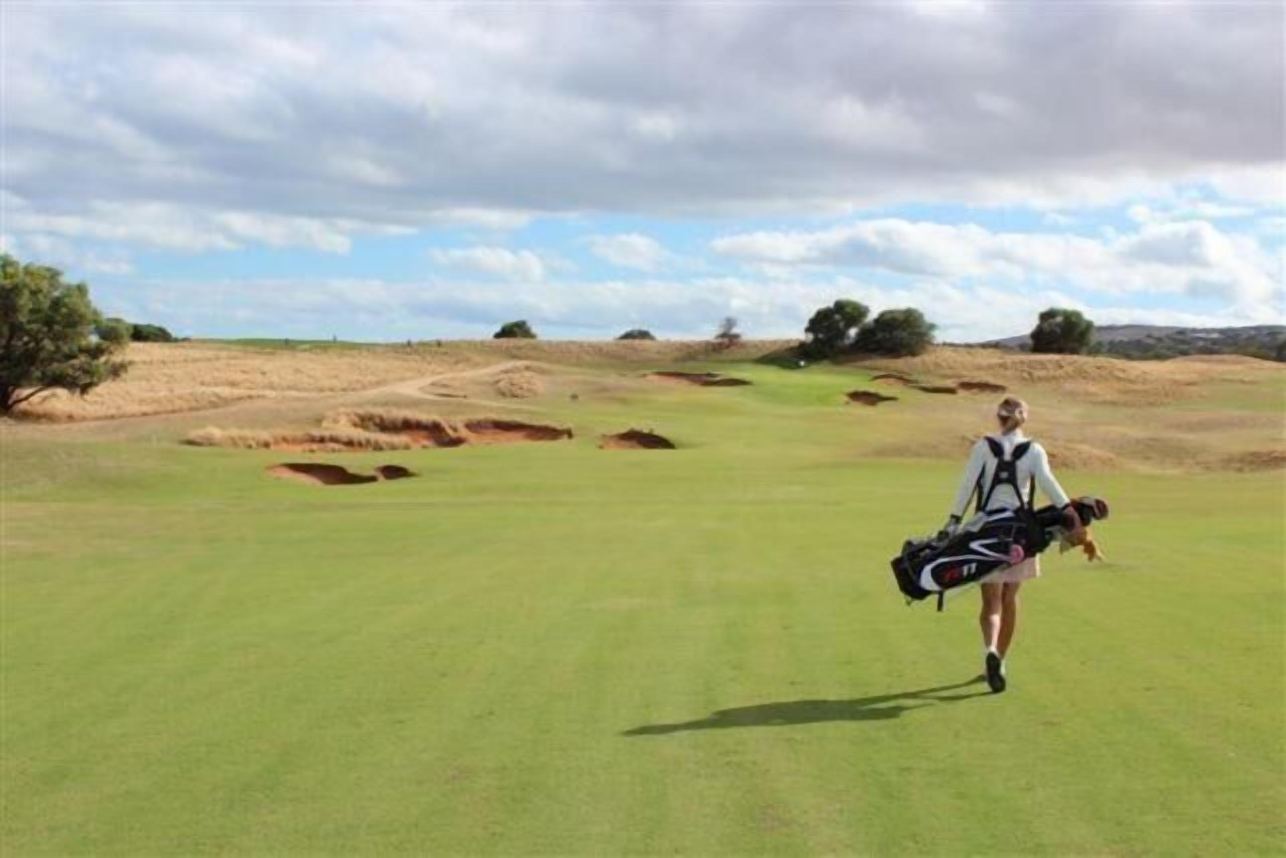 Un campo de golf bajo un cielo despejado y una persona cargando un bolso de golf.
